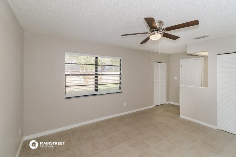 the spacious living room with a large window and a ceiling fan