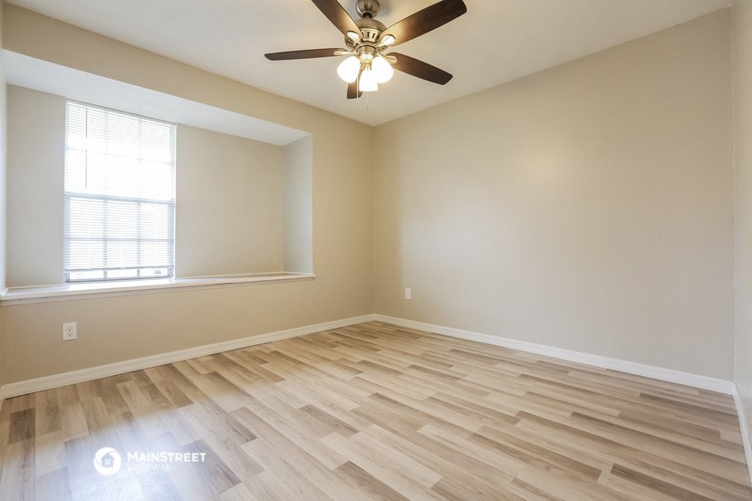 the spacious living room with hardwood flooring and a ceiling fan