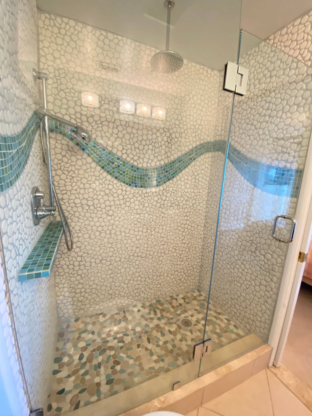 a large shower with a glass door and pebbles on the floor