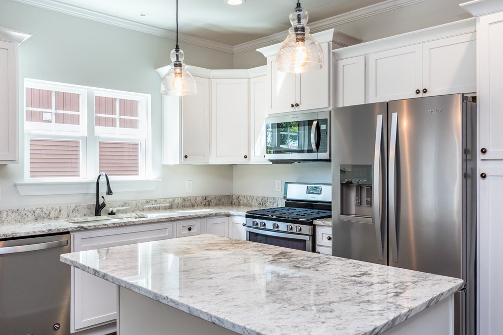 a white kitchen with stainless steel appliances and marble counter tops