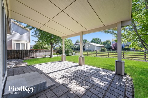 a covered patio with a lawn and a house in the background