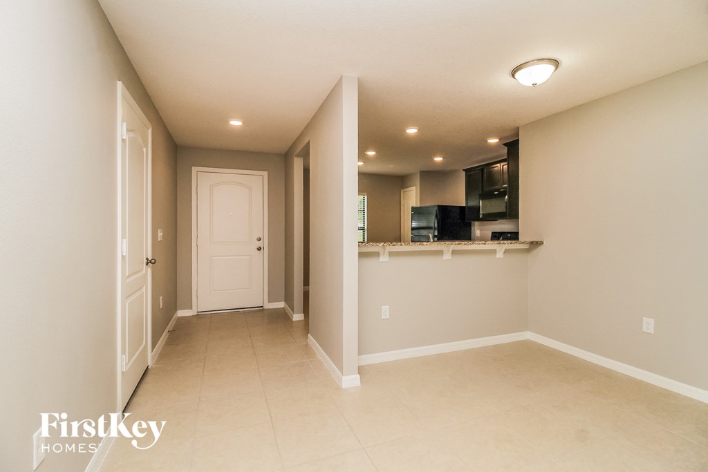 an empty living room with a kitchen and a door to a hallway