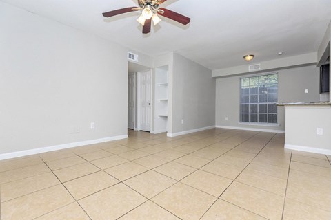 an empty living room with a ceiling fan and tiled floors