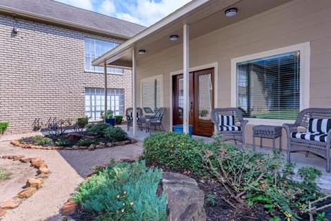 the front porch of a home with rocking chairs and a garden