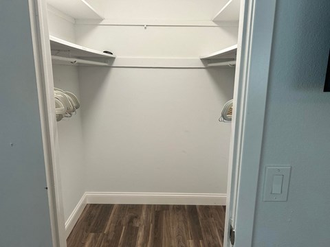 a walk in closet with white walls and wood floors