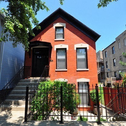a small red brick house with a black fence