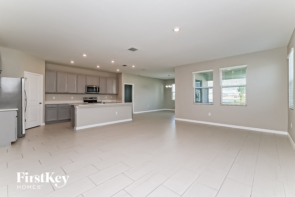 an open kitchen and living room with white tile flooring and stainless steel appliances