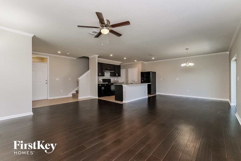an empty living room and kitchen with wood flooring and a ceiling fan