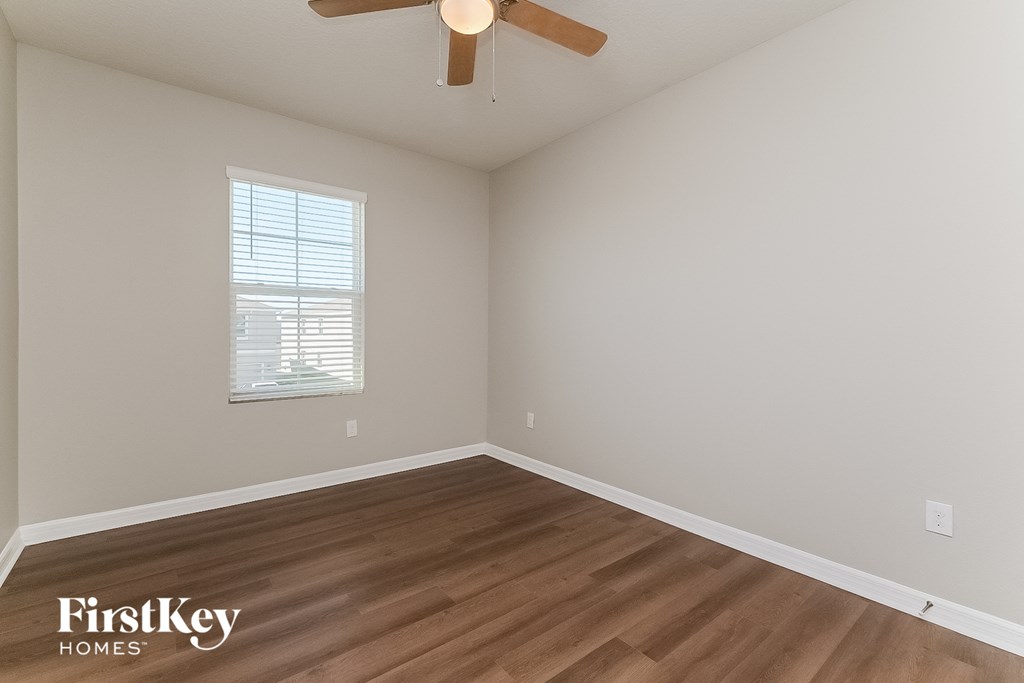 the spacious living room with hardwood flooring and a ceiling fan