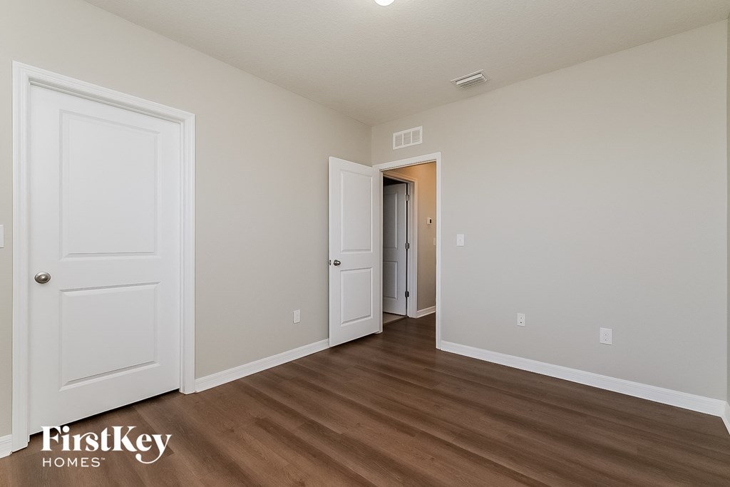 a bedroom with white walls and wood flooring and a door to a hallway