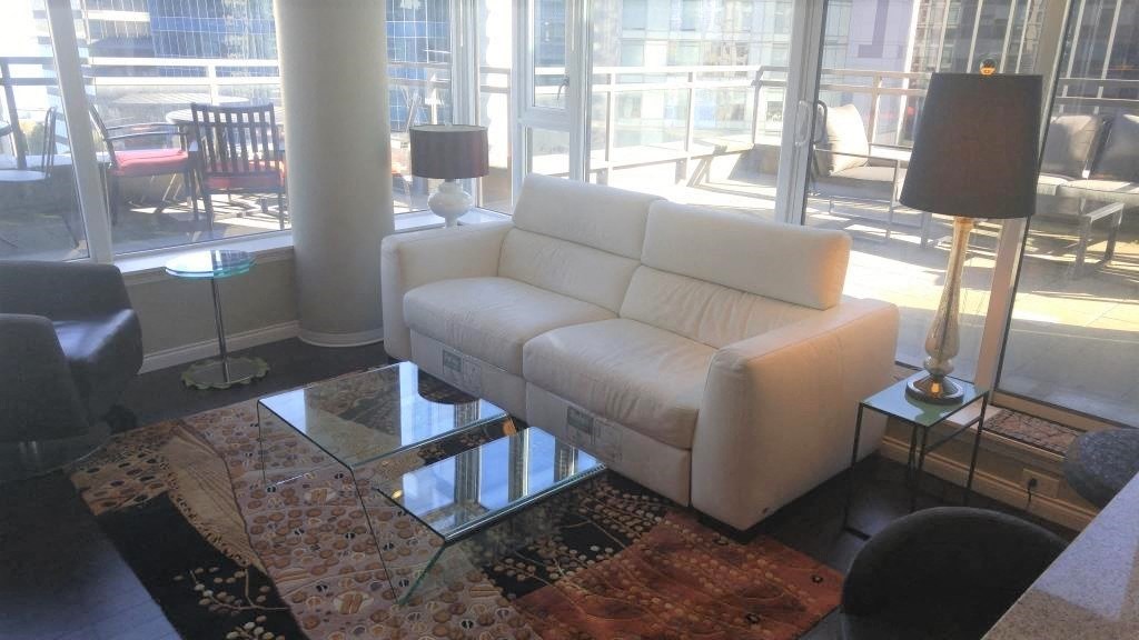 A white couch sits in a room with a glass table and a lamp.