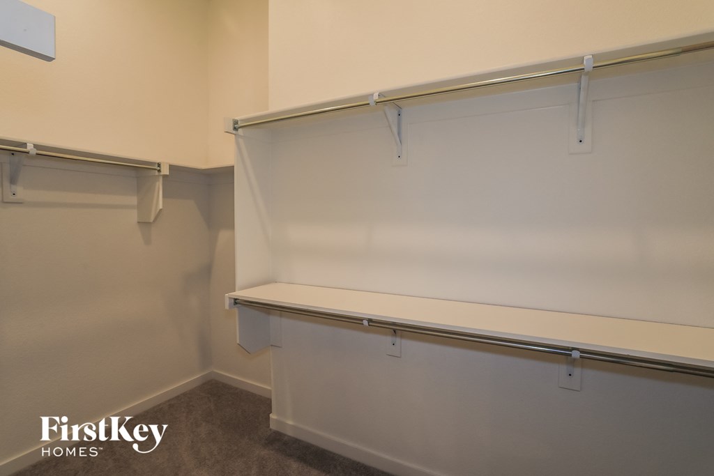 a walk in closet in an empty room with a white wall and a white bench