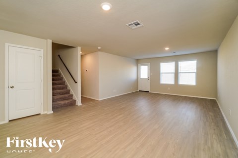 A spacious room with wooden flooring and a staircase leading to another room.