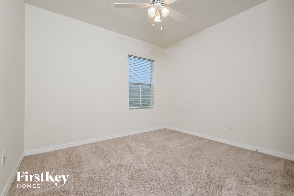 the spacious living room with carpeted flooring and a ceiling fan