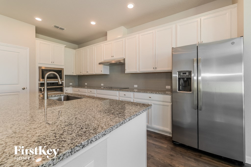 a white kitchen with granite counter tops and stainless steel refrigerator