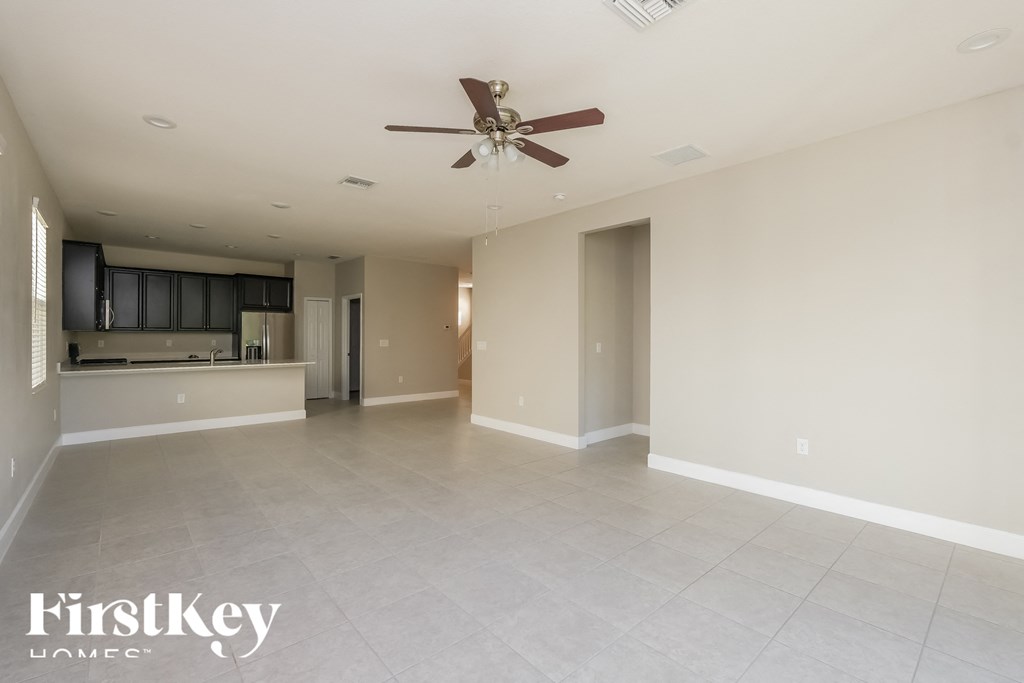 an empty living room with a ceiling fan and a kitchen