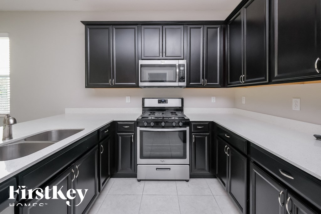 a kitchen with black cabinets and white counter tops and a stove and microwave