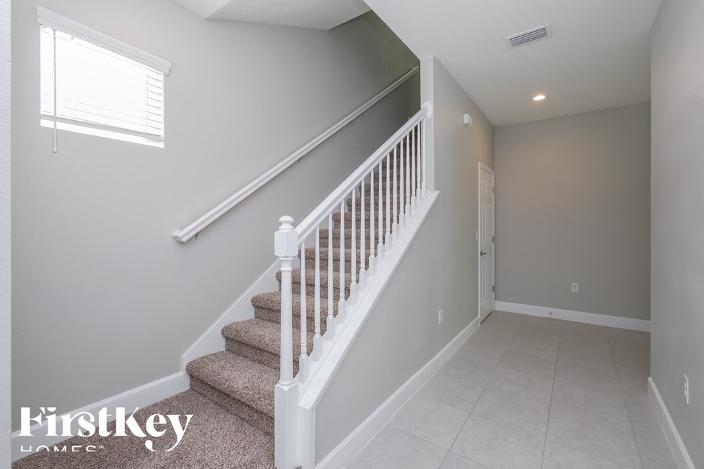 a staircase in a home with grey walls and a white railing and a window