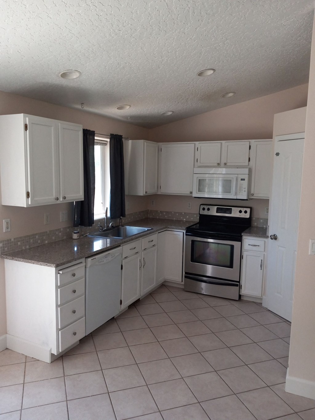 an empty kitchen with white cabinets and stainless steel appliances