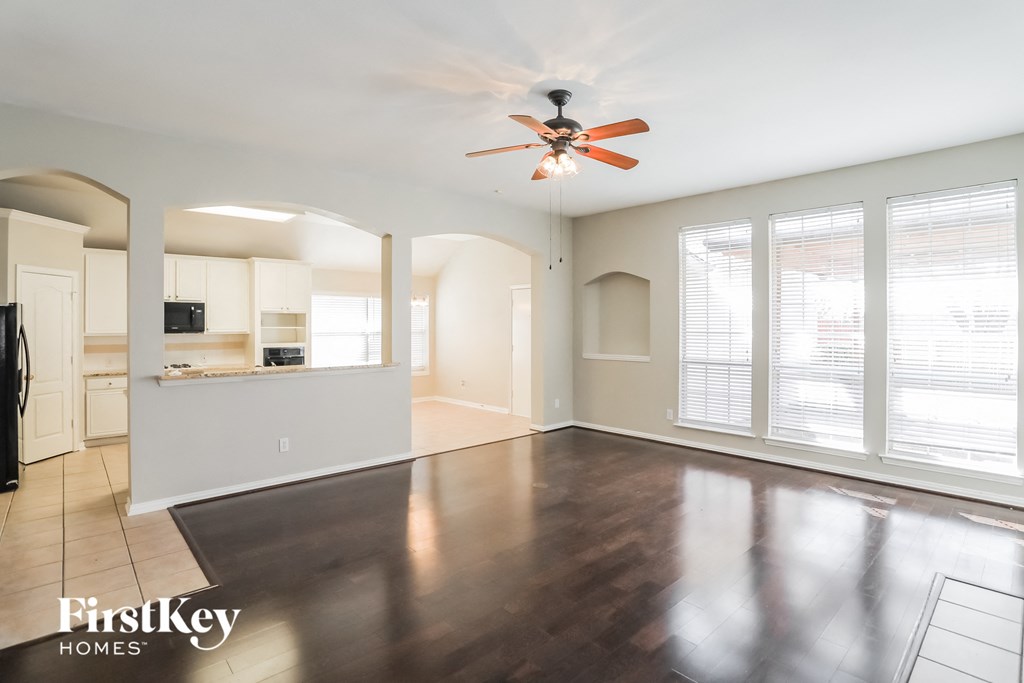 an empty living room with a ceiling fan and a kitchen