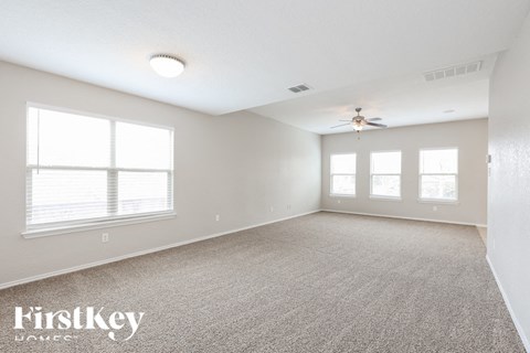 A spacious room with a carpeted floor, a ceiling fan, and three windows.