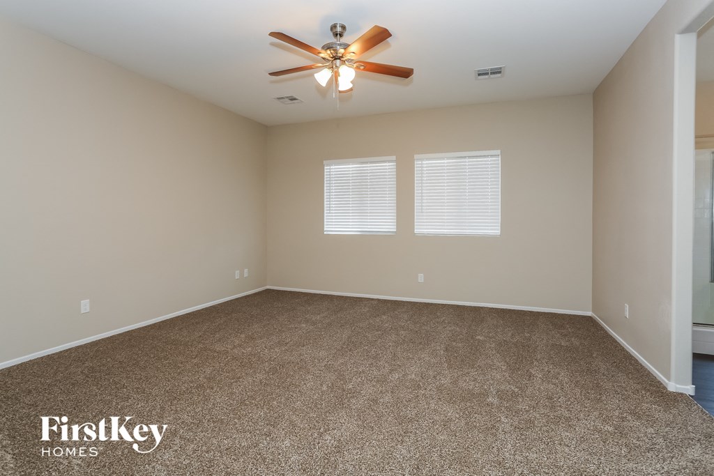 A room with a carpeted floor, a ceiling fan, and two windows with blinds.
