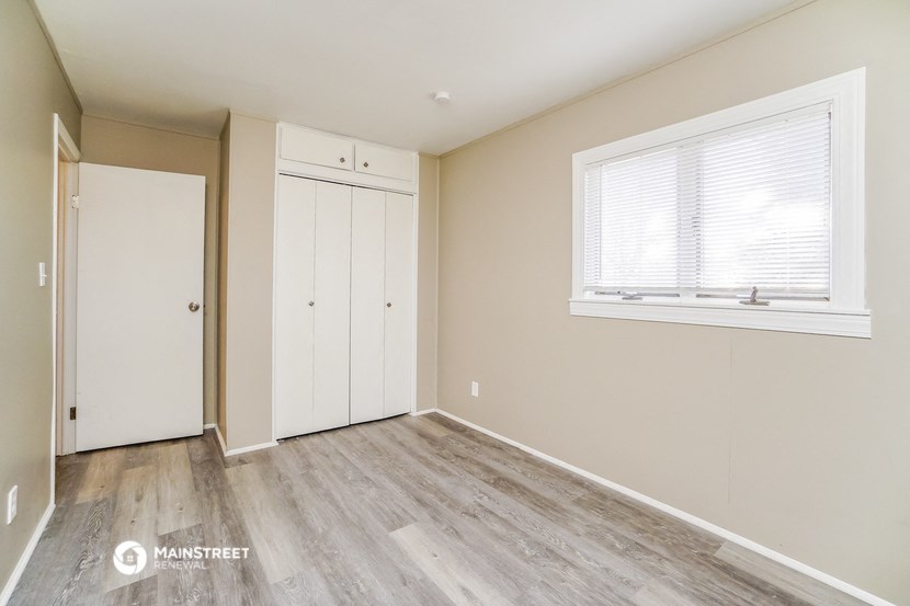 a bedroom with white walls and wood floors and a window