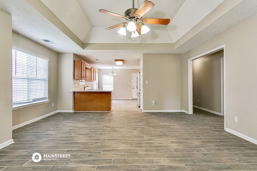 an empty living room with a ceiling fan and a kitchen