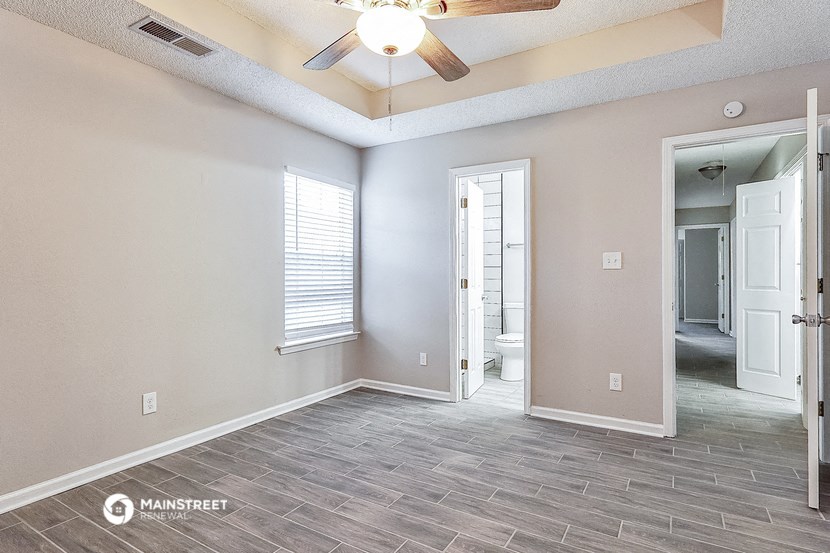 an empty living room with a ceiling fan and a door to a bathroom