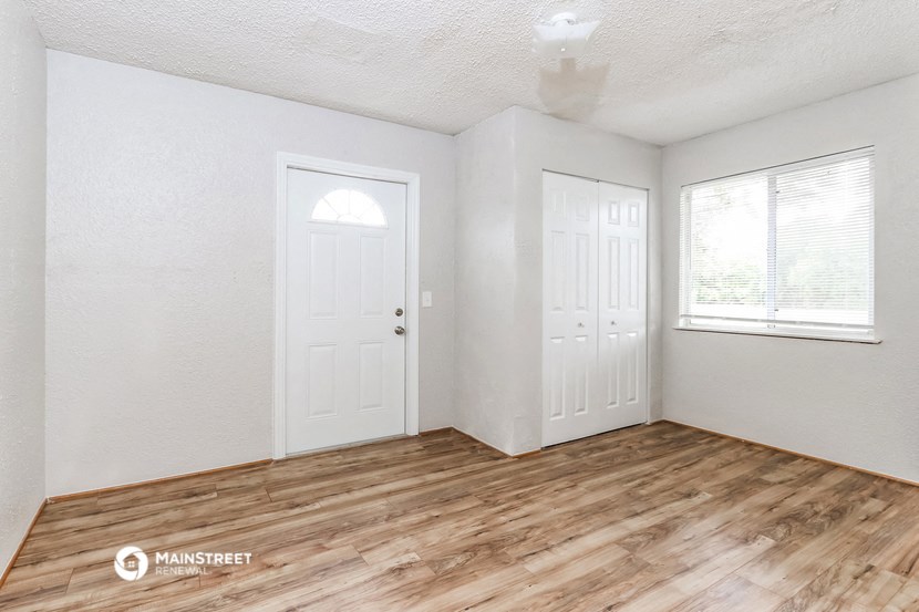 the living room of a small white house with wood flooring and two doors