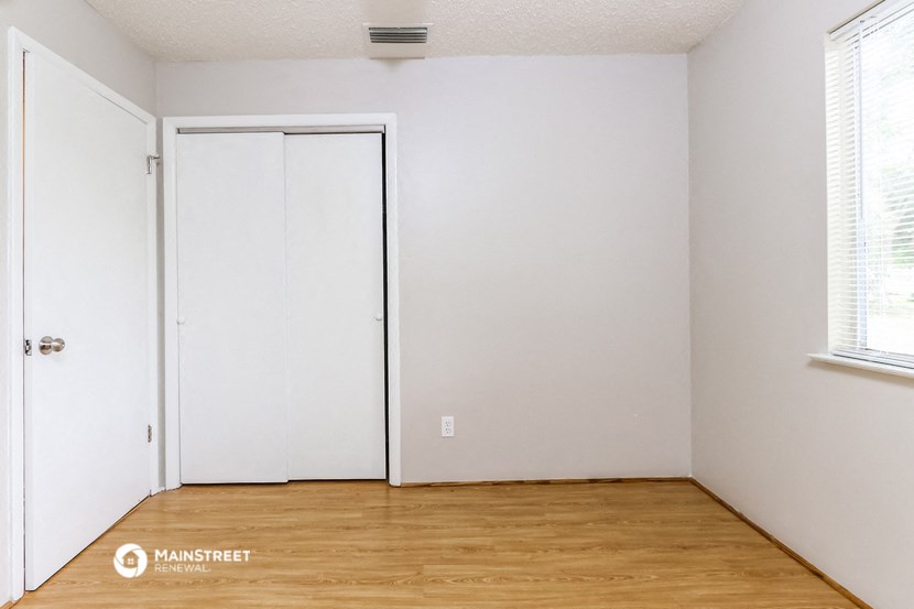 a bedroom with white walls and a wooden floor and a closet