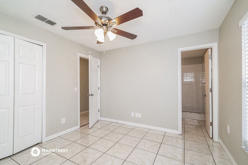 an empty living room with a ceiling fan and a door to a bathroom