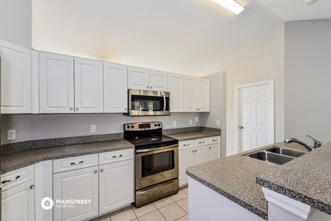 the kitchen has granite counter tops and white cabinets and stainless steel appliances