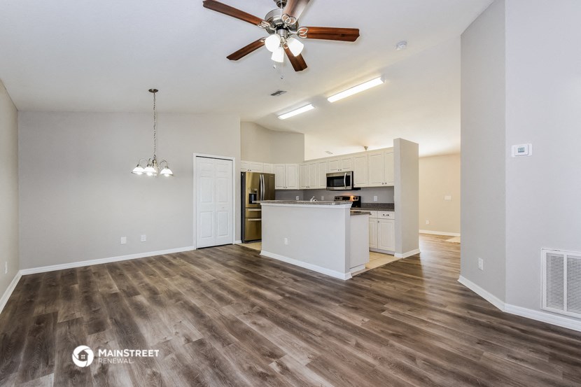 the living room and kitchen of an apartment with wood flooring and a ceiling fan