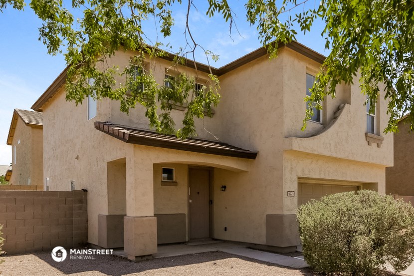 the front of a tan house with a garage door and a tree