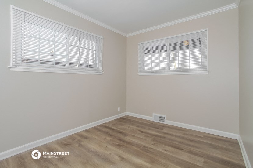 a bedroom with wood floors and two windows