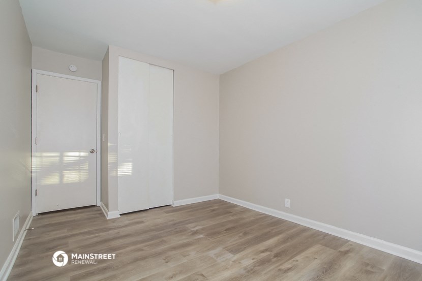 a bedroom with white walls and wood flooring and a closet