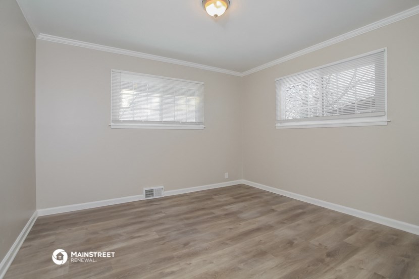 the interior of an empty room with wood flooring and two windows