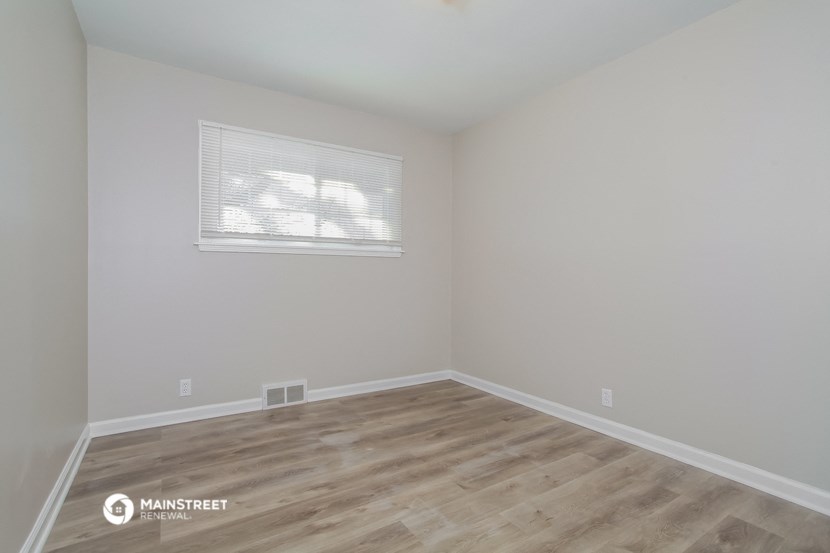 a bedroom with wood floors and white walls and a window