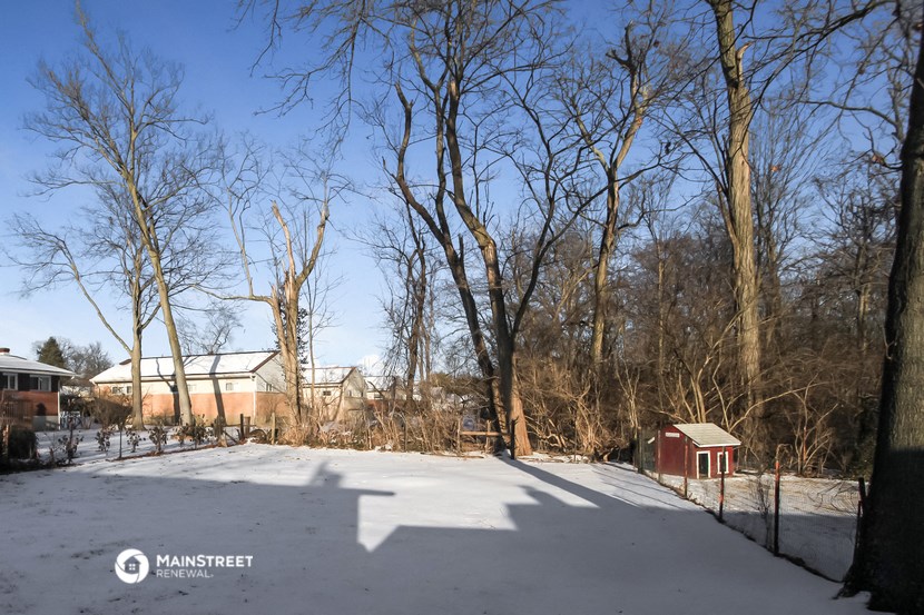 a yard covered in snow with trees and a house in the background