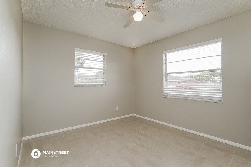 the spacious living room with two windows and a ceiling fan