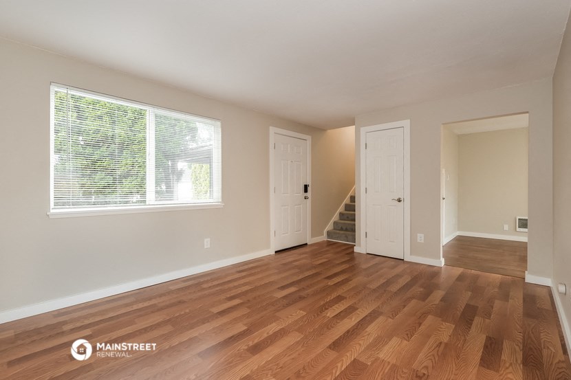 the living room of a house with a large window and wooden floors