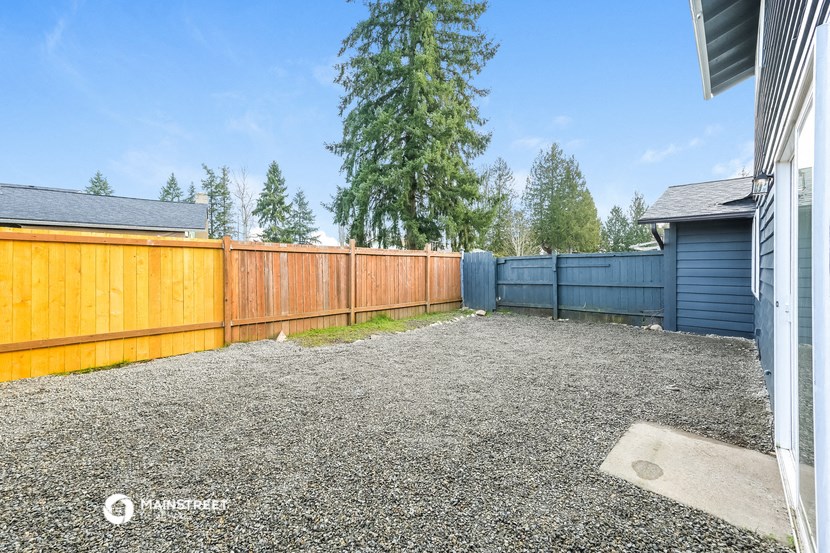 the backyard of a house with a wooden fence and a pine tree