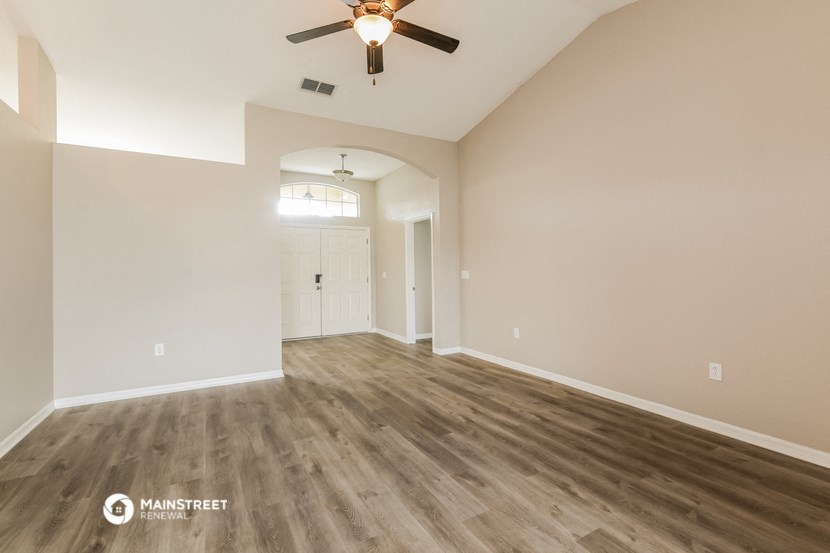 the spacious living room with hardwood flooring and a ceiling fan