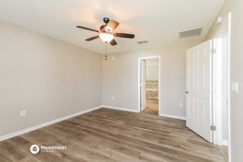 the spacious living room with ceiling fan and white walls
