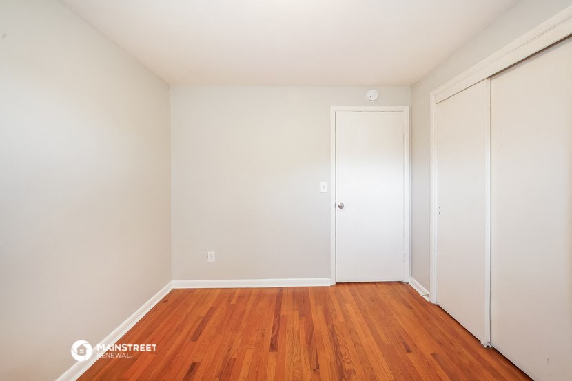 a bedroom with white walls and wood floors and a closet