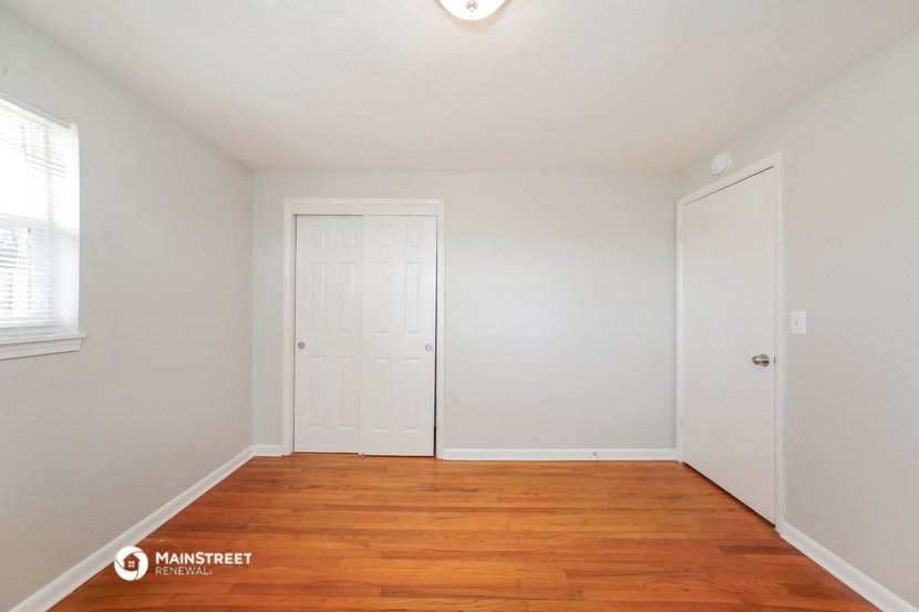 a bedroom with white walls and wood flooring and a closet