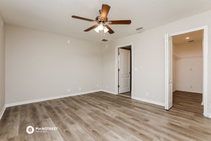 the spacious living room with ceiling fan and white walls