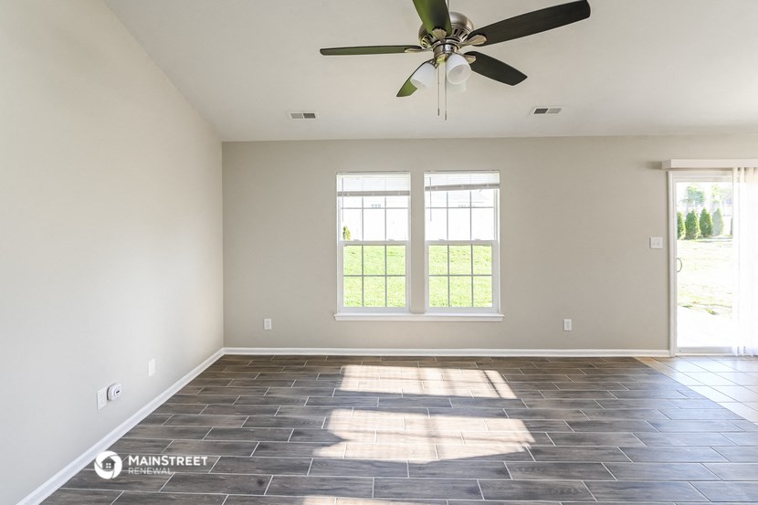 an empty living room with a ceiling fan and two windows