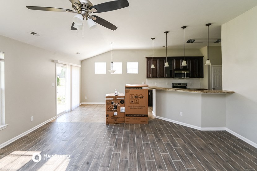an empty living room with boxes on the floor and a kitchen